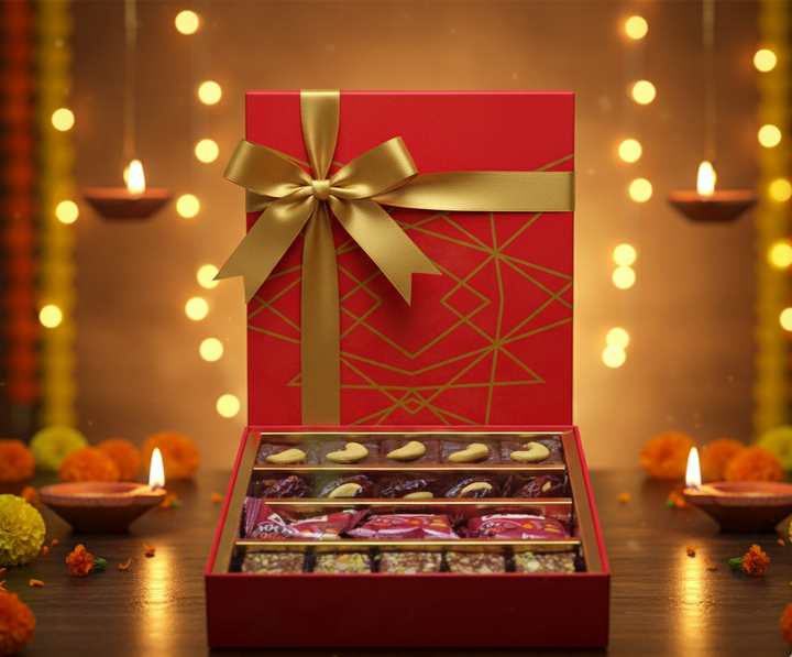 Red gift box with gold bow and chocolate assortment on a festive background with lights and candles.
